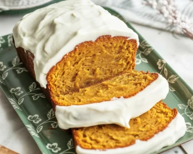 Slices of pumpkin loaf topped with cream cheese frosting on a plate, perfect for fall.