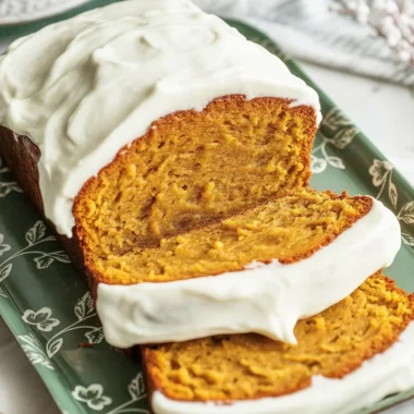 Slices of pumpkin loaf topped with cream cheese frosting on a plate, perfect for fall.