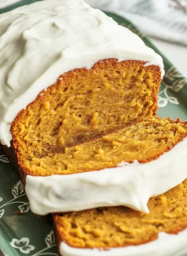 Slices of pumpkin loaf topped with cream cheese frosting on a plate, perfect for fall.