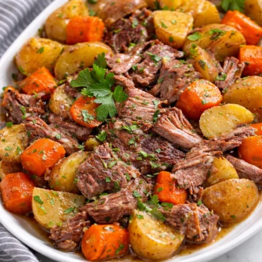 Delicious Slow Cooker Pot Roast with Potatoes, Carrots, and rich beef broth served on platter.