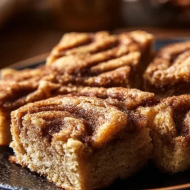 Cinnamon Swirl Snickerdoodle Blondies stacked on a plate with a sprinkle of cinnamon