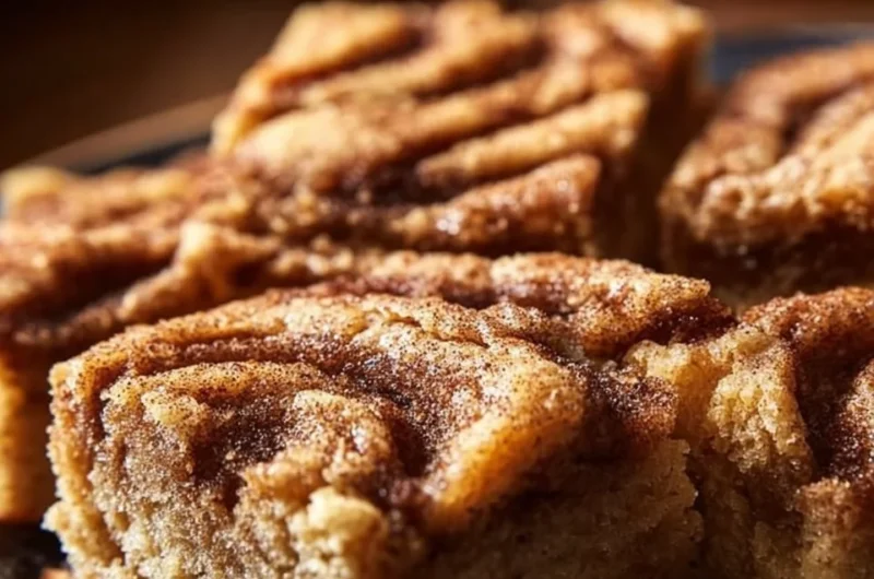 Cinnamon Swirl Snickerdoodle Blondies stacked on a plate with a sprinkle of cinnamon