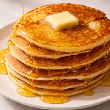 Delicious stack of fluffy homemade pancakes served with fresh fruits on a plate.