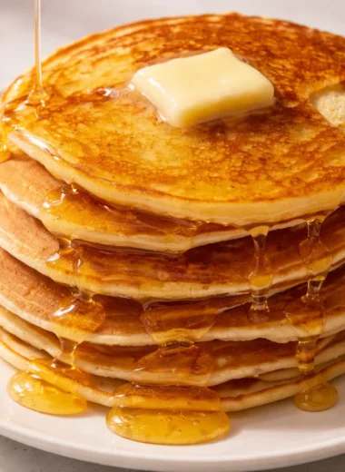 Delicious stack of fluffy homemade pancakes served with fresh fruits on a plate.