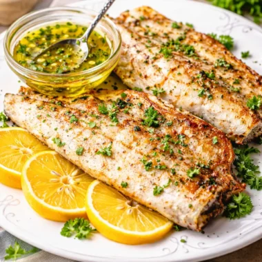 Grilled barramundi fillets with lemon butter sauce on a plate.