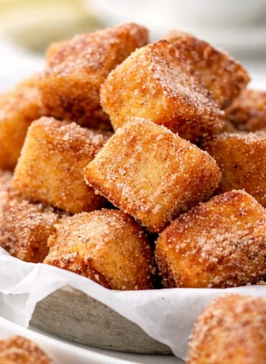 Bite-sized Cinnamon Roll French Toast Bites arranged on a plate with syrup drizzle.
