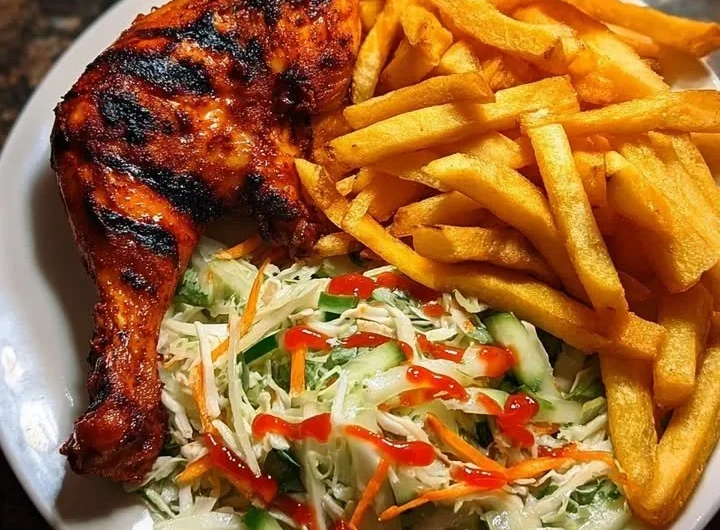 Crispy fries served with flame-grilled chicken leg and salad on a plate.