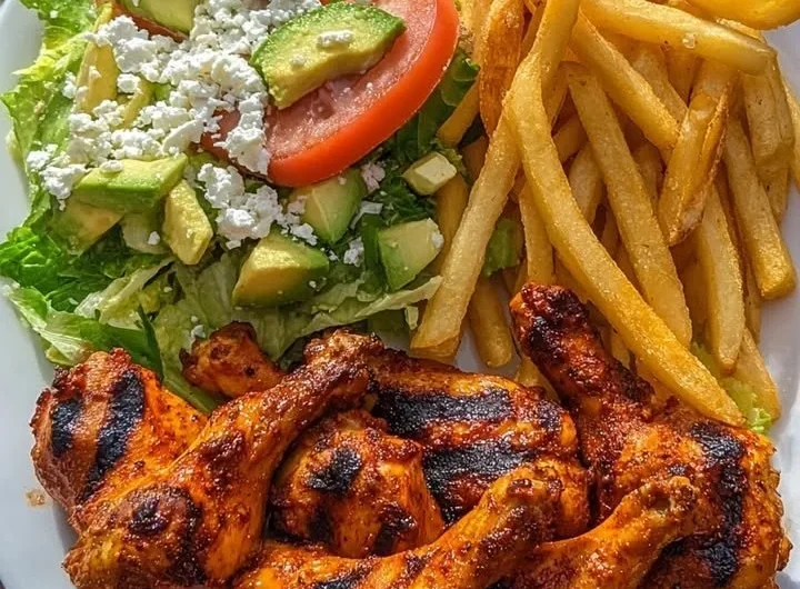 Crispy grilled chicken drumsticks with fries and avocado salad on a plate