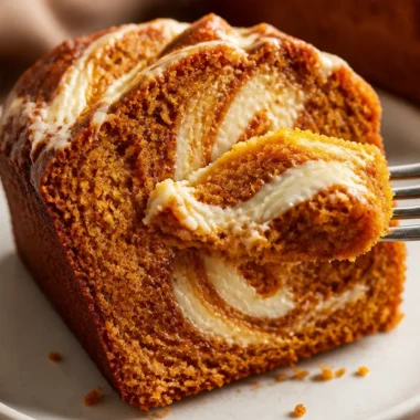 Delicious pumpkin bread with cream cheese swirl on a rustic wooden table.