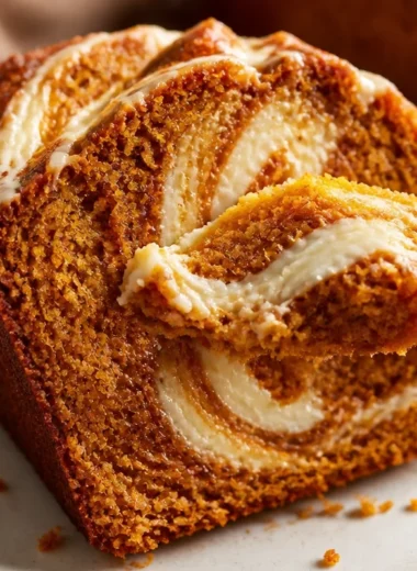 Delicious pumpkin bread with cream cheese swirl on a rustic wooden table.