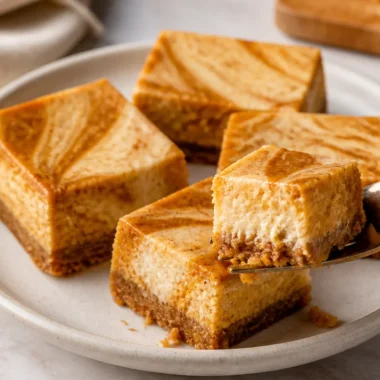 Delicious pumpkin cheesecake bars topped with whipped cream and spices