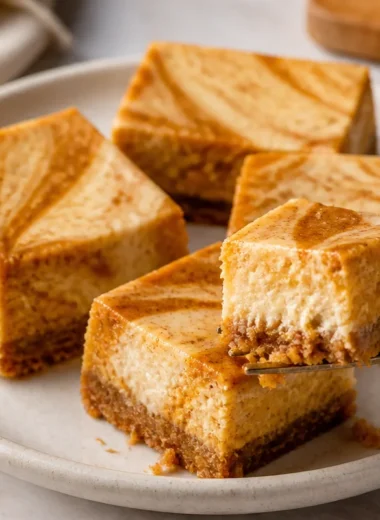 Delicious pumpkin cheesecake bars topped with whipped cream and spices